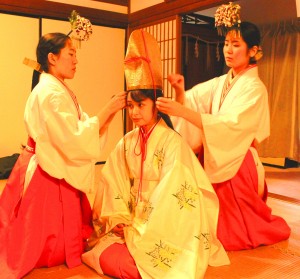 巫女に金烏帽子装束を着せてもらう福娘