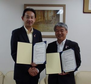 協定書を手に握手する濱田市長と森川村長（右）