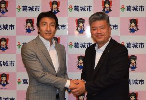 葛城市スポーツアドバイザーに就任した朝原宣治さん（左）と握手する山下市長