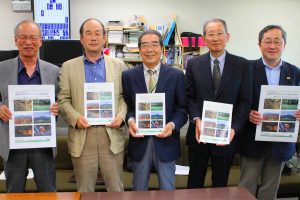 ５周年の記念誌を持つ小北博孝理事長（中央）ら