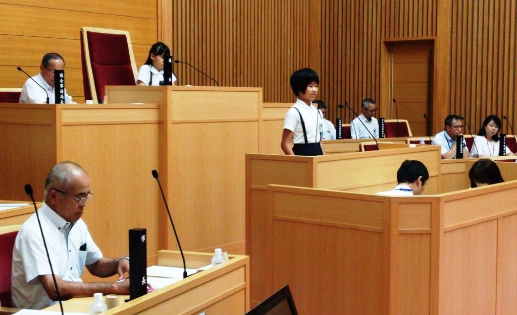 竹内幹郎市長（手前左）に議場で質問する小学生