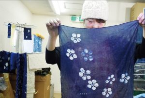 映画「あい」の中で、あい染め作品の出来を確認する女性出演者(ピース・クリエイト提供)