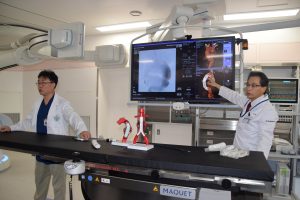 手術室に備えられた血管撮影が行える最新鋭の医療機器の説明を行う医師ら